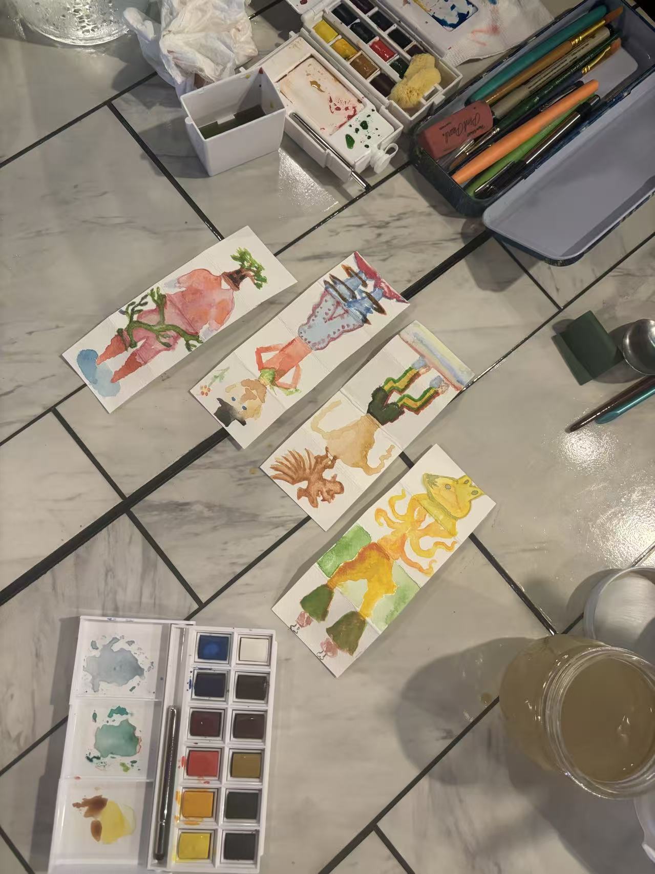 Book club artwork and watercolor supplies spread across a table